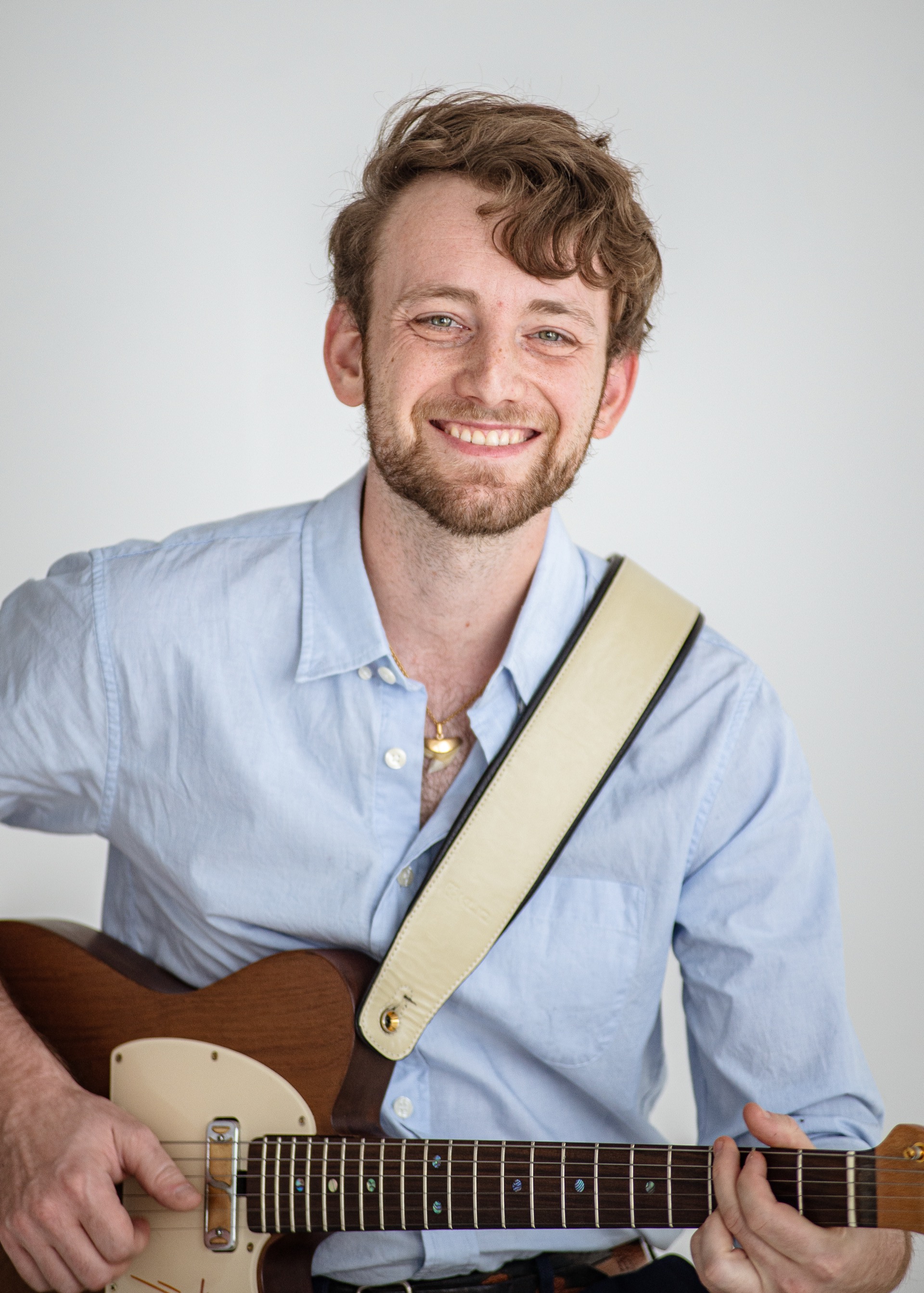 Jordan Lovinger headshot — smiling with guitar, looking up