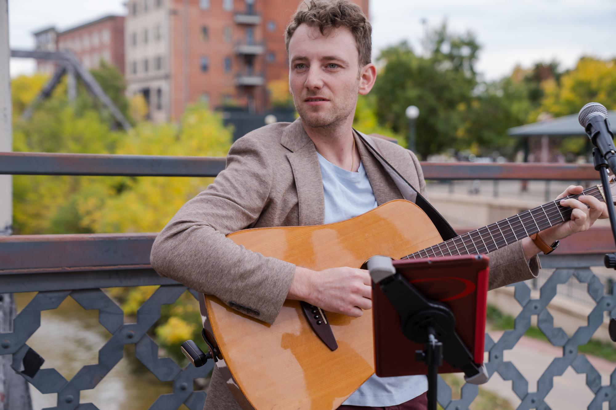 Jordan Lovinger in professional attire performing guitar at a Colorado wedding ceremony on Coohills bridge